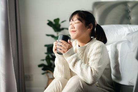 Young woman drinking coffee in bedroom, Holding coffee cup with two hands
