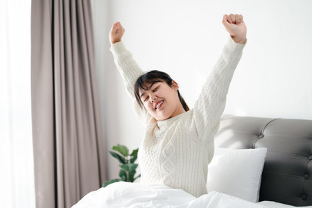Happy Woman stretching her arms on the bed in the morning.の写真素材