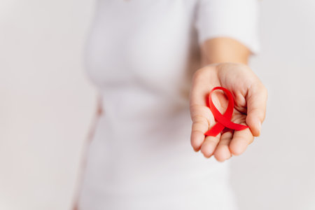 Closeup woman hand holding red ribbon HIV, world AIDS day awareness ribbon. Healthcare and medicine concept.の写真素材