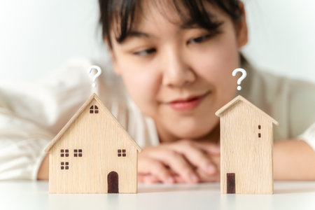 woman is deciding to choose house with Small Wooden House Model with Question Marks, Planning to buy property. Choose what's the best. home loan concepts.の写真素材