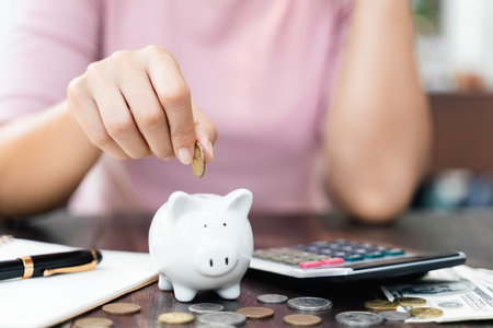 Closeup of woman hand putting money coin into piggy bank for saving money. saving money and...