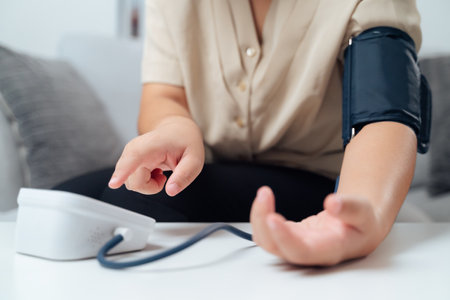 A woman is sitting on a couch with a blood pressure monitor on her arm. She is checking her blood pressure and she is concerned about the resultsの写真素材