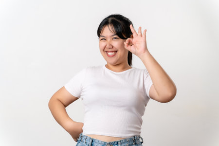 A woman is smiling and giving the OK sign gesture.. She is wearing a white shirt and blue jeansの写真素材