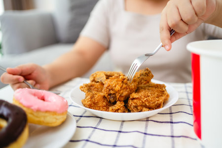 A woman is happily eating fried chicken and donuts on a plate. She is sitting in a living room.の写真素材