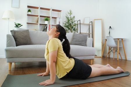 Asian woman stretching muscles with a yoga pose on a yoga mat in a living room at home.の写真素材