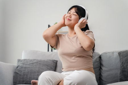Asian woman listening to music happily, having fun and relaxing with headphones in living room at home, relaxation and hobby concept.の写真素材