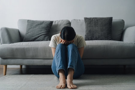 A woman is sitting on the floor in a living room. She is crying and she is in a state of distressの写真素材