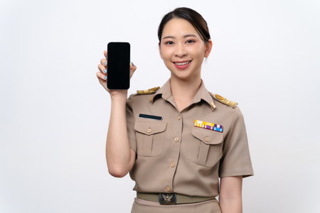 A beautiful Thai Asian Teacher in the uniform shows a blank screen of mobile phone. She smiles at the camera with a happy attitude.の写真素材