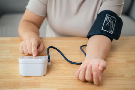 An Asian woman uses a portable blood pressure monitor in her living room. Health awareness concept.の写真素材
