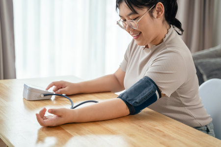 An Asian woman uses a portable blood pressure monitor in her living room. Health awareness concept.