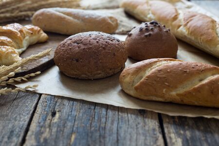 Different kinds of fresh baked bread on old wooden table background