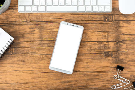 office desk with smartphone blank screen, computer and office supplies top view