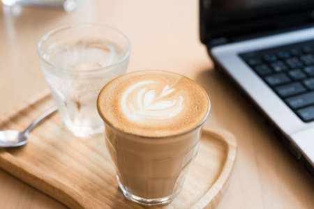 coffee cup latte art with cake and laptop computer on a wooden table in a coffee shop.の写真素材