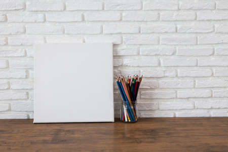 Empty white canvas frame and color pencils on a wooden tableの写真素材