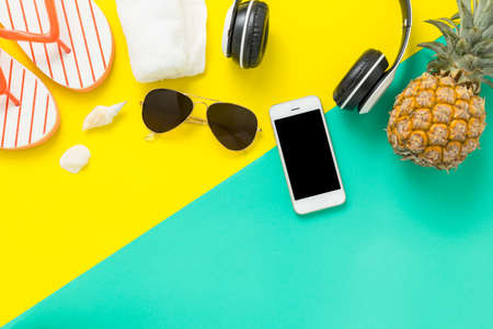 Summer Holidays background Concept, Phone with pineapple, glasses and flip flops On a green and yellow background top viewの写真素材