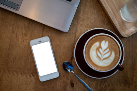 Blank screen smart phone and computer on wooden table top view In the coffee shop