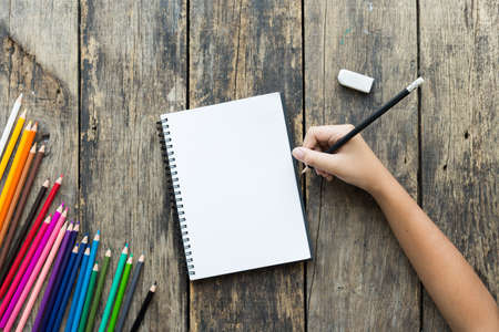 Girl hand drawing, blank paper and colorful pencils on old wooden tableの写真素材