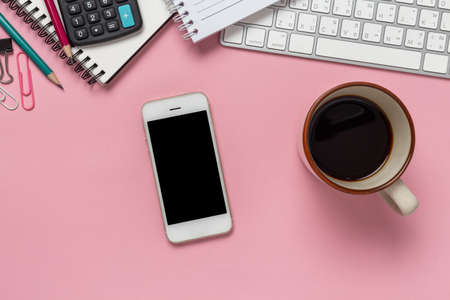 Top view office desk with empty smartphone, computer and office supplies on a pink background