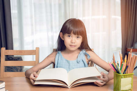 Child girl reading a book on the table in the house