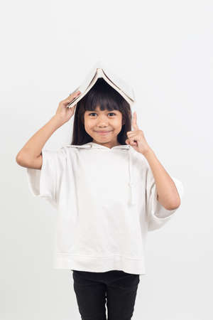 Portrait of asian little girl put the book on the head. Then use your upward hand.の写真素材