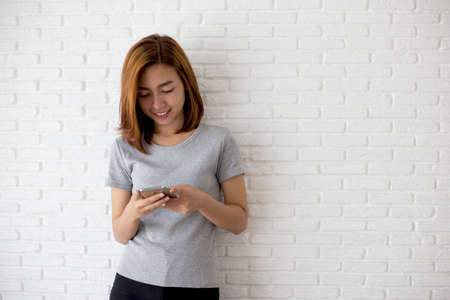 Young woman using smart phone at brick wall white background.の写真素材