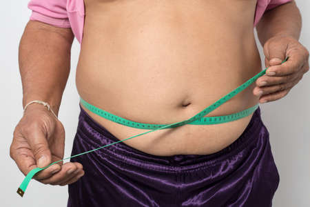 Overweight man check out his body fat with green measuring tape for obesity on gray background, Healthy conceptの写真素材