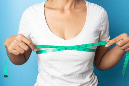 Close up of young woman measuring her bust size with green measuring tape on a blue backgroundの写真素材