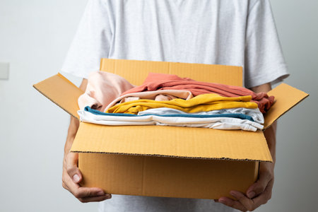 Donation Concept, man holding clothes with donate box in white background room.