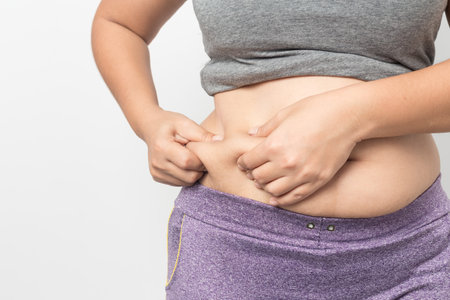 Overweight woman hand pinching excessive belly fat on gray background, Healthy conceptの写真素材