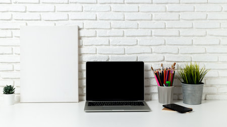 mockup laptop computer with blank white screen, with workspace and office supplies on a wooden desk