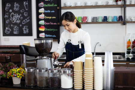 Female barista in an apron stands behind a bar counter in a cafe,
Woman barista preparing a coffee shop for customers.の写真素材