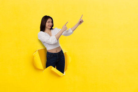 Happy Asian woman smiling with thumbs up pointing at empty space Stand on a hole in the middle of the yellow paper.の写真素材
