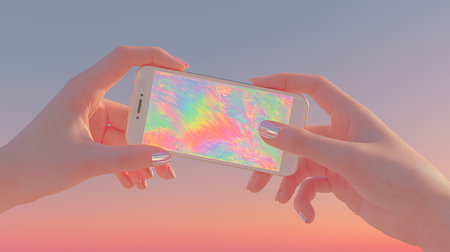 Hands holding a smartphone with a colorful screen on the background of the sunsetの素材