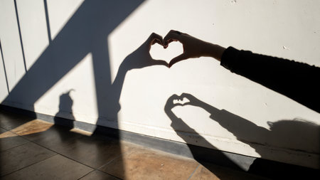 Female hands forming a heart shape on a white wall with shadow.の素材