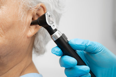 Otolaryngologist or ENT physician doctor examining senior patient ear with otoscope, hearing loss problem.の写真素材