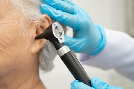 Otolaryngologist or ENT physician doctor examining senior patient ear with otoscope, hearing loss...