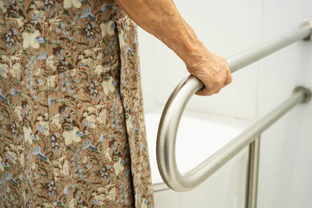 Asian elderly woman patient use toilet support rail in bathroom.