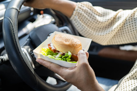 Asian woman driver holding hamburger in car.