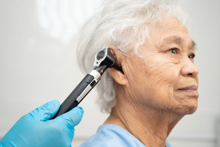 Otolaryngologist or ENT physician doctor examining senior patient ear with otoscope, hearing loss...