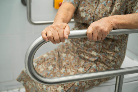 Asian elderly woman patient use toilet support rail in bathroom.