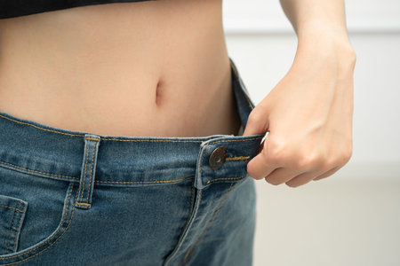 Young Asian woman losing weight wearing loose pants in oversize jeans.