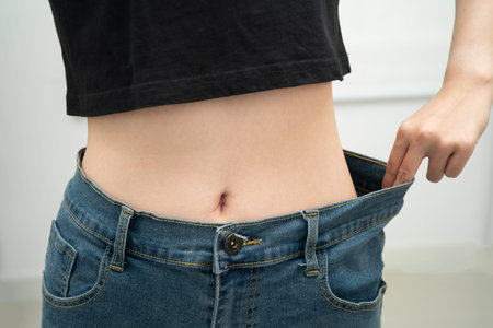 Young Asian woman losing weight wearing loose pants in oversize jeans.