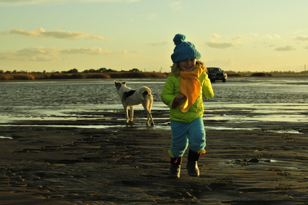 Running  little girl  on a sunset sandy autumn beach. Sunset on the coast of the Ladoga Lakeの写真素材