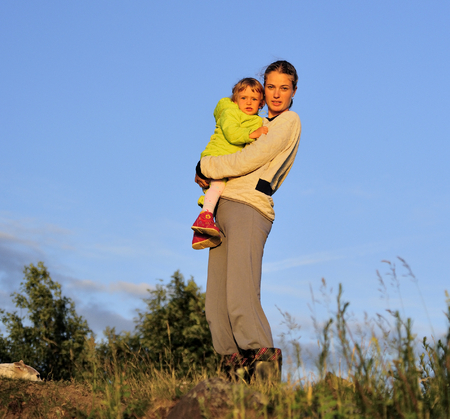 Young Attractive young mother holding a little girl in her arms at sunset light.  Walk in the autumn warm evening outdoors at sunset. Solar flare lights Woman and child.の写真素材
