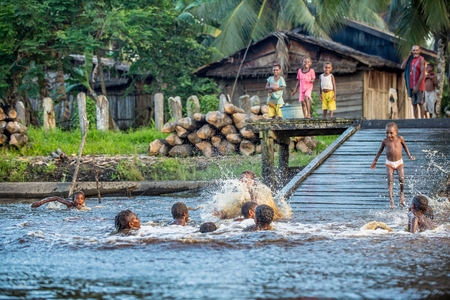 YOUW VILLAGE, ATSY DISTRICT, ASMAT REGION, IRIAN JAYA, NEW GUINEA, INDONESIA - MAY 23, 2016: Noisy fun kids. Children of the tribe of Asmat people bathe and swim in the river. New Guinea.May 23, 2016のeditorial素材