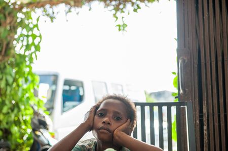 WEST PAPUA (IRIAN JAYA), ASMAT PROVINCE, NEW GUINEA, INDONESIA - MAY 22, 2016: - Unidentified boy of an asmat tribe on bright background, frame of green plants. New Guinea Island. May 22, 2016のeditorial素材
