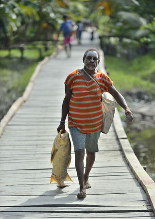 YOUW VILLAGE, ATSY DISTRICT, ASMAT REGION, IRIAN JAYA, NEW GUINEA, INDONESIA - MAY 23, 2016: Woman with fish. Portrait of a woman from the tribe of Asmat people. Village of Asmat people. New Guinea.のeditorial素材