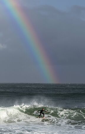 Mossel Bay, South Africa - July 17 2019: Surfing the waves. Surfer riding wave with rainbow on storm...