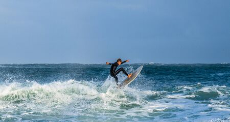 Mossel Bay, South Africa - July 17 2019: Surfing the waves. Surfer riding wave with rainbow on storm...