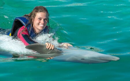 Smiling woman swimming with dolphin in blue water.の写真素材